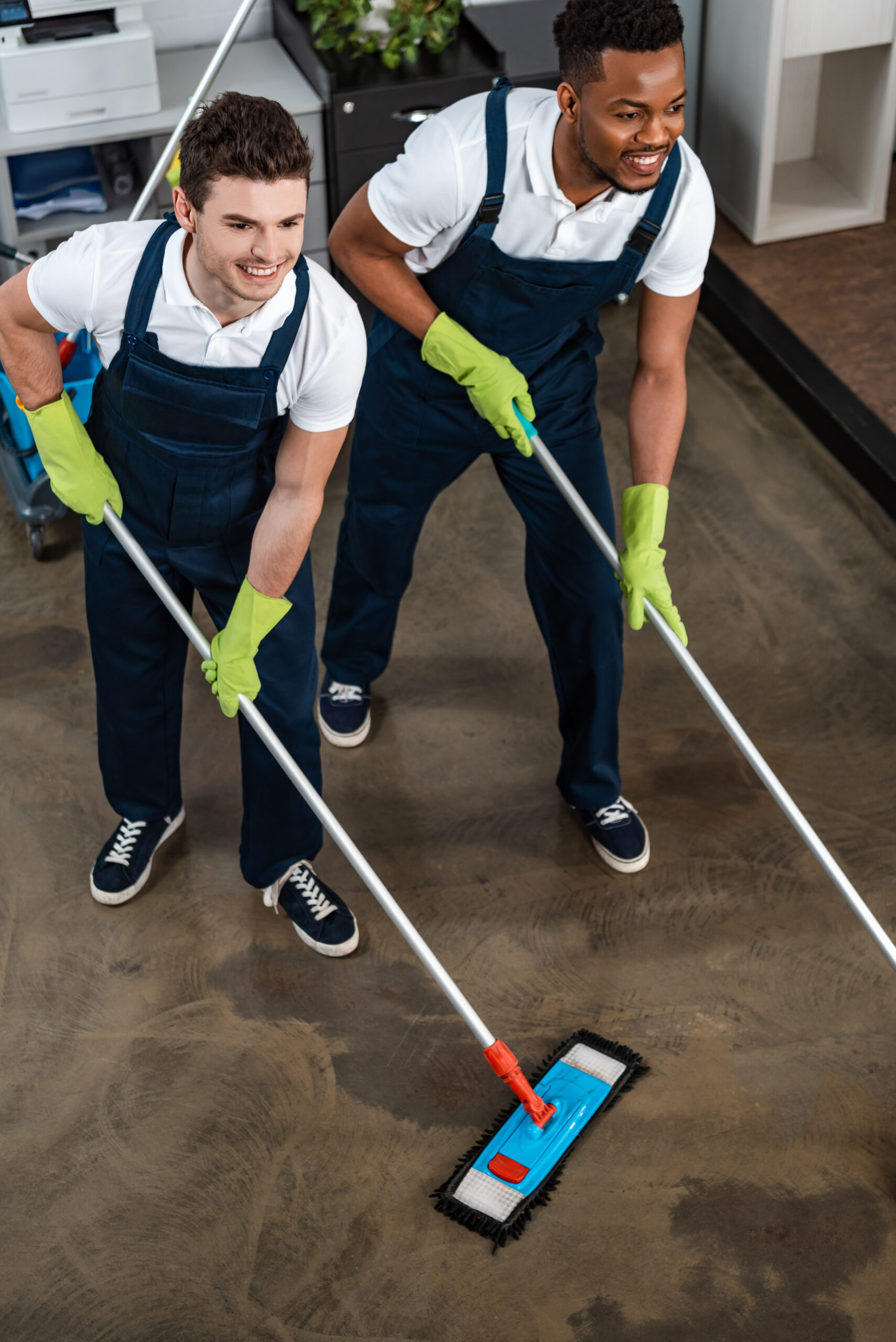 two smiling multicultural cleaners washing floor with mops